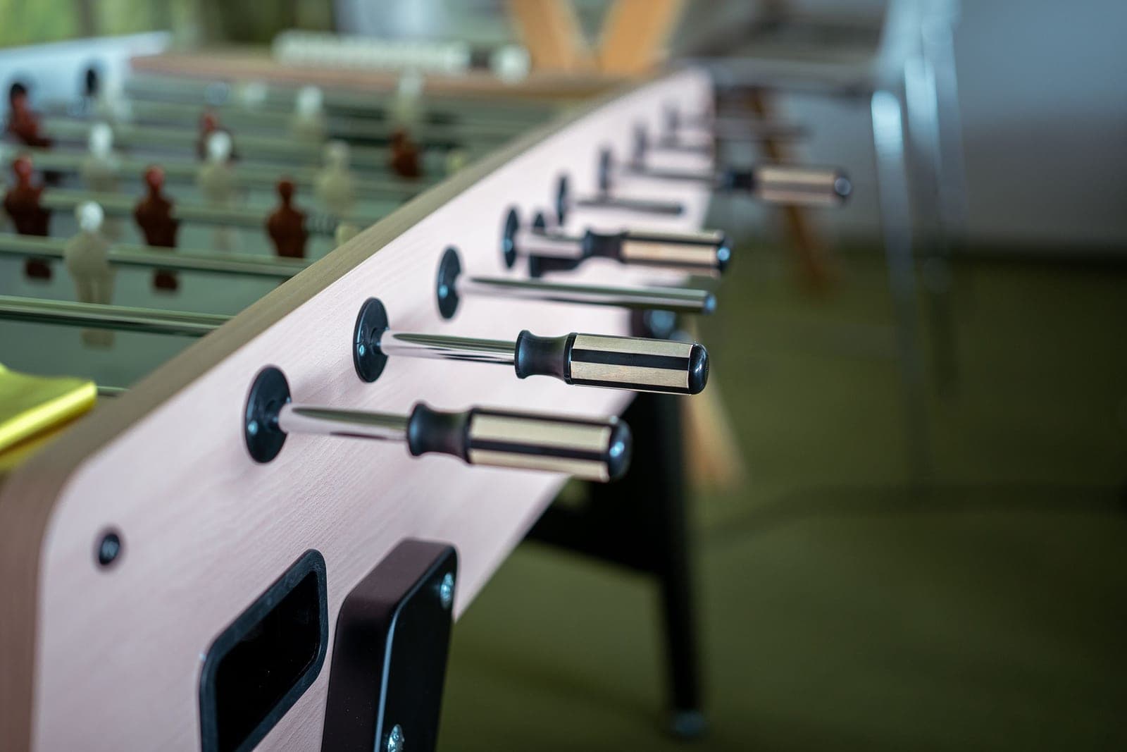 A foosball table in a games room with a player's hands on the rods and clear floor on both sides
